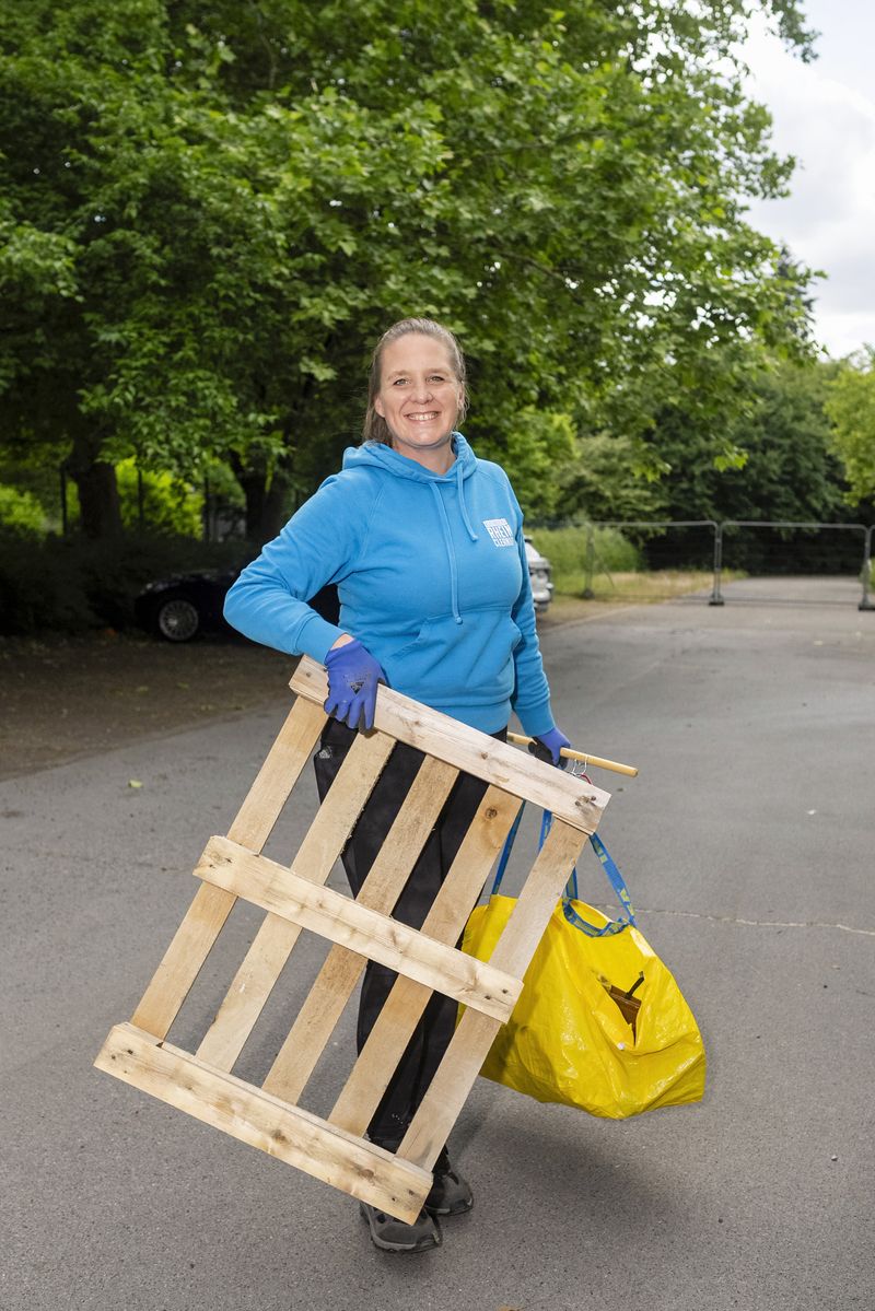 Eine Frau trägt eine Holzpalette und eine gelbe Tasche in einem Park.